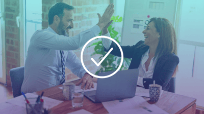 Two workers high fiving while sat at a desk