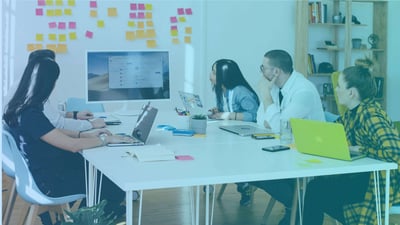 Employees sitting around a desk, looking at a screen