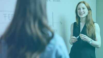 Woman standing by a whiteboard, speaking to another woman