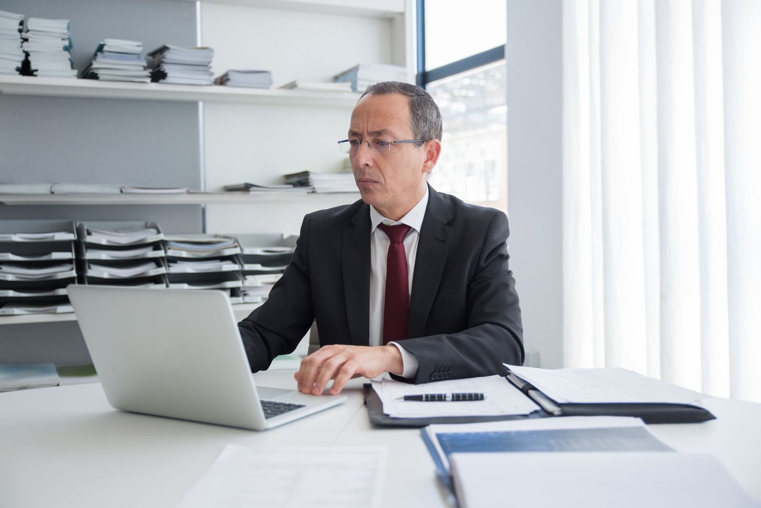Business man in suit, sitting at a desk and typing on a laptop