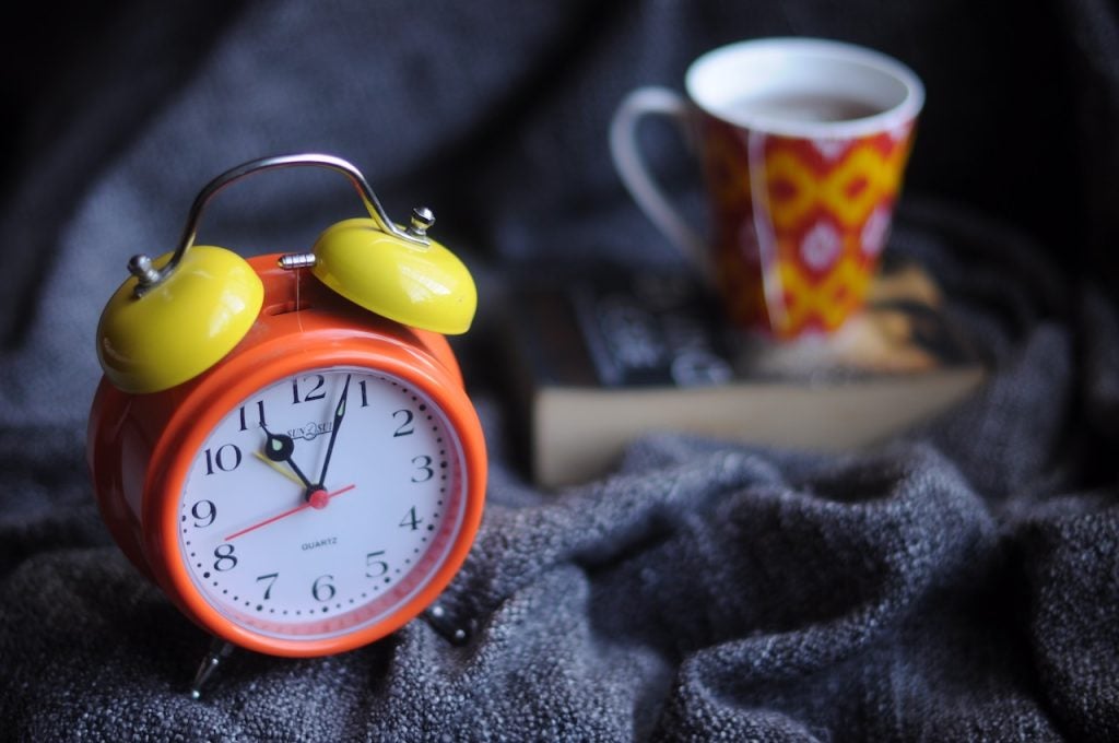 orange-alarm-clock-next-to-orange-mug-and-book-on-blanket