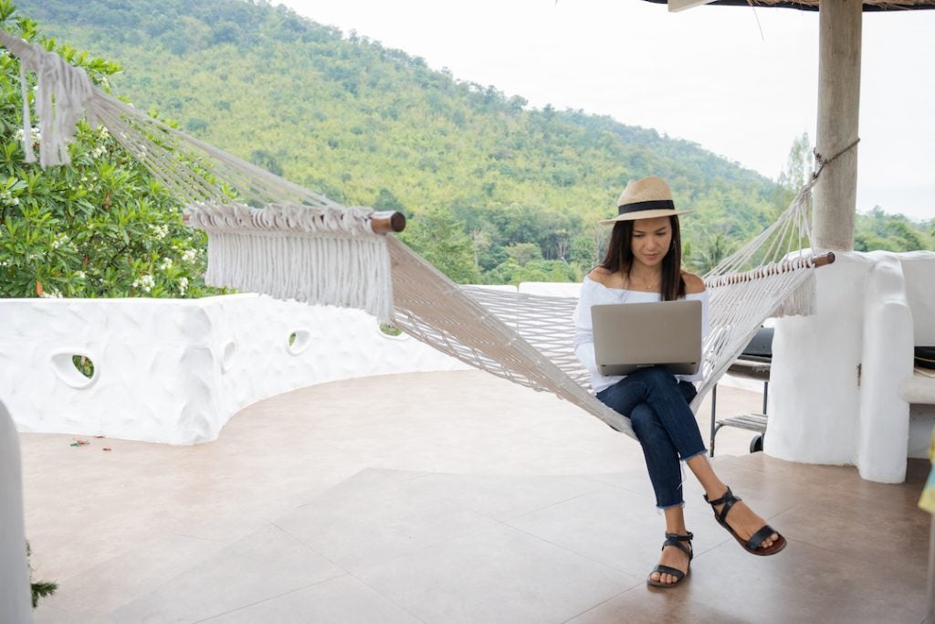female-working-remotely-sitting-on-hammock-with-mountains-in-background
