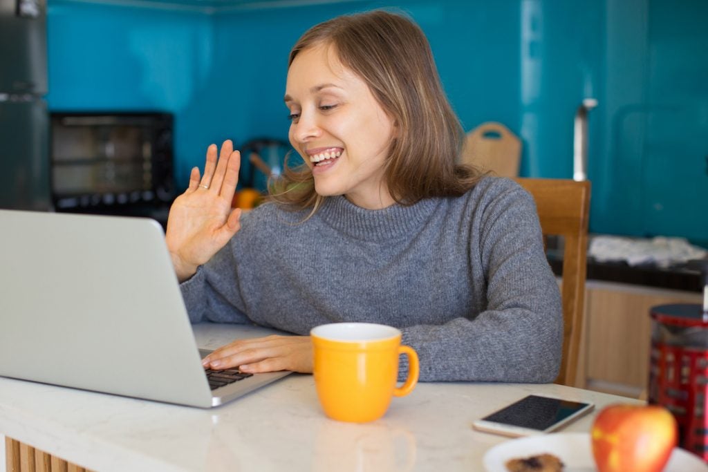 woman-working-from-home-waving-during-video-meeting